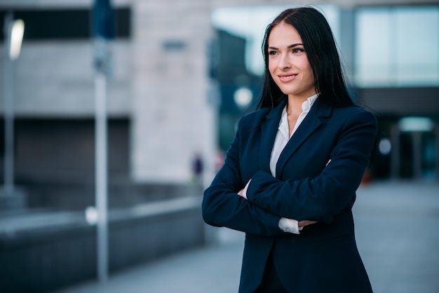 Portrait de femme d'affaires souriante en costume, centre d'affaires. Bâtiment financier moderne, paysage urbain.