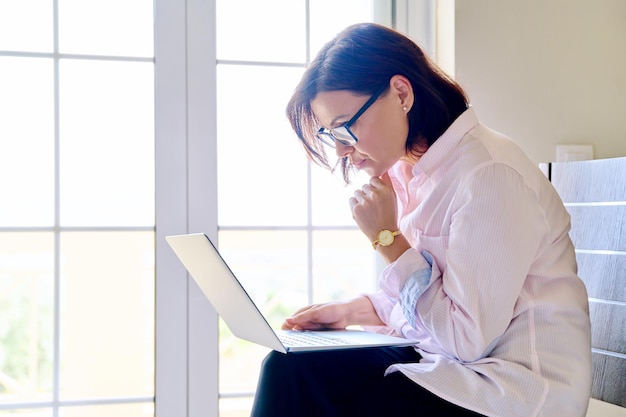 Portrait d'une femme d'affaires travaillant avec un ordinateur portable assis sur une chaise au bureau