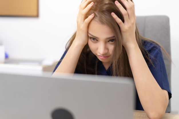 Portrait de femme d'affaires travaillant tout en utilisant un ordinateur portable sur certains rapports de la maison alors qu'il est fatigué et stressé. Femme d'affaires multitâche et stress.