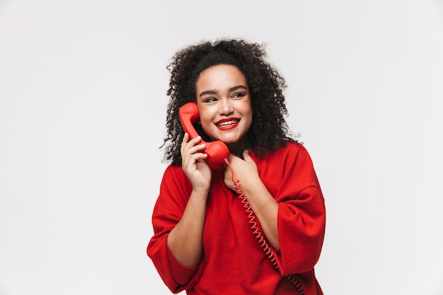 Portrait d'une femme africaine joyeuse debout isolée sur fond blanc, parlant sur un téléphone fixe