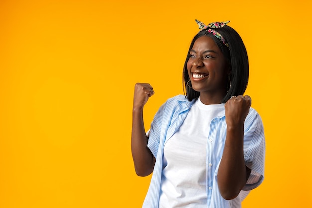 Portrait d'une femme africaine joyeuse avec les mains levées sur fond jaune