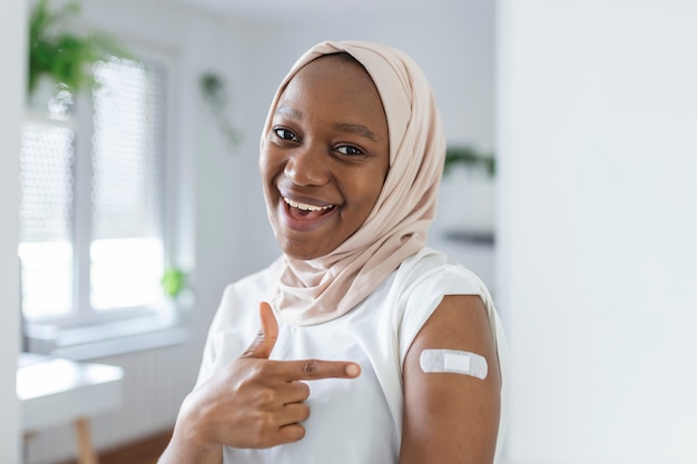 Portrait d'une femme africaine musulmane souriante après avoir reçu un vaccin. Femme tenant sa manche de chemise et montrant son bras avec un bandage après avoir reçu la vaccination.