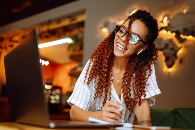 Portrait d'une femme afro-américaine assise au café ayant un appel vidéo sur un ordinateur portable