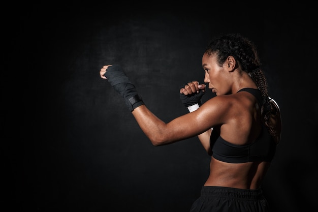 Portrait d'une femme afro-américaine en bonne santé portant des vêtements de sport boxe dans des enveloppements à la main isolés sur fond noir