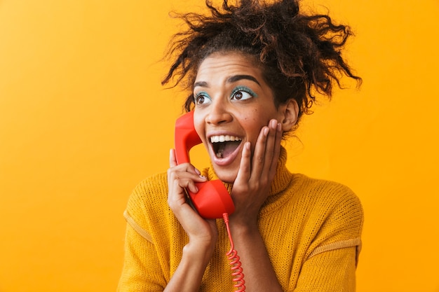 Photo portrait de femme afro-américaine excitée avec une coiffure afro souriant et tenant un combiné rouge, isolé