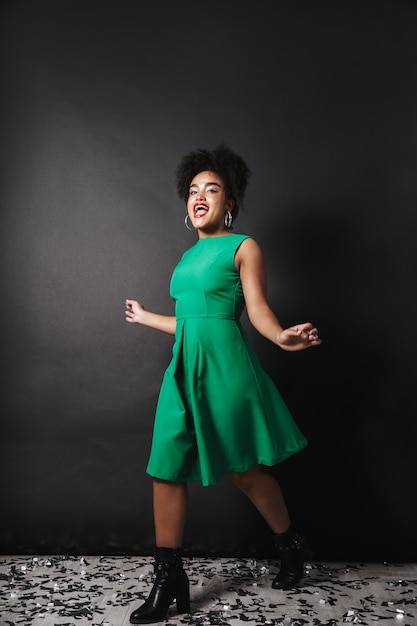 Portrait d'une femme afro-américaine joyeuse portant une robe debout sur un mur noir