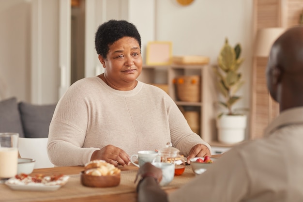 Portrait de femme afro-américaine senior assis à table à manger pendant le petit-déjeuner en famille à la maison