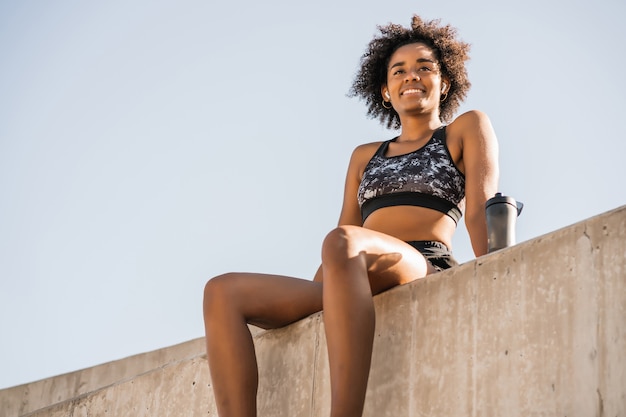 Portrait d'une femme afro-athlète relaxante et assise après le travail à l'extérieur. Sport et mode de vie sain.
