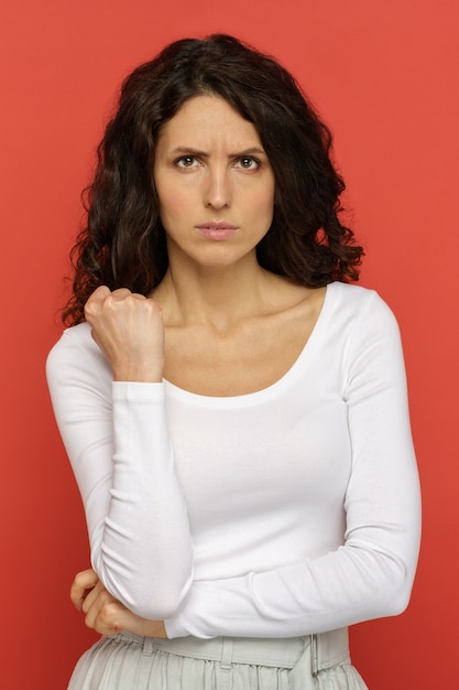 Portrait d'une femme agacée en colère montrant le poing à la caméra donner un stand d'avertissement avec la main pliée au mur rouge