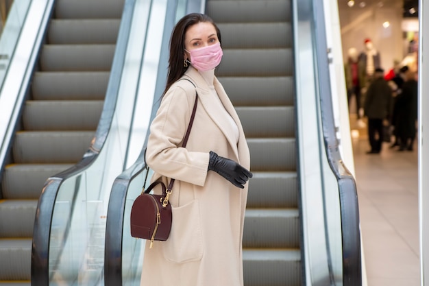 Portrait d'une femme d'âge moyen avec des gants et un masque sur l'escalator dans un lieu public