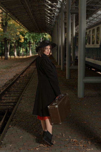 Portrait d'une femme d'âge moyen en manteau et chapeau Dame vintage avec valise rétro attendant le train à la gare