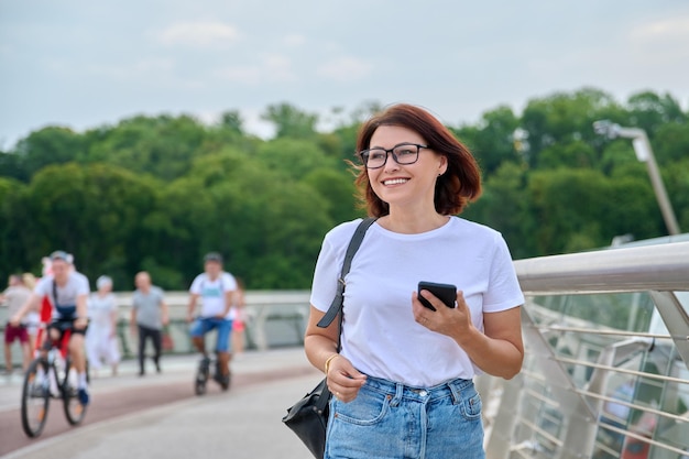 Portrait d'une femme d'âge moyen marchant avec un smartphone à la main journée d'été en ville