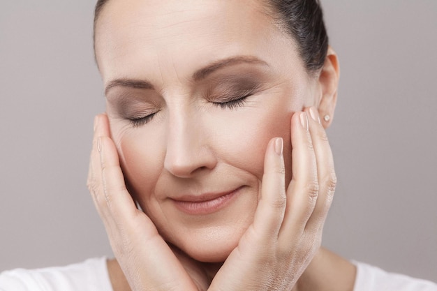 Portrait d'une femme d'âge moyen satisfaite avec une relaxation parfaite de la peau du visage après une procédure de spa avec les yeux fermés isolés sur fond gris. Concept de beauté et de soins de la peau, espace de copie, prise de vue en studio, intérieur