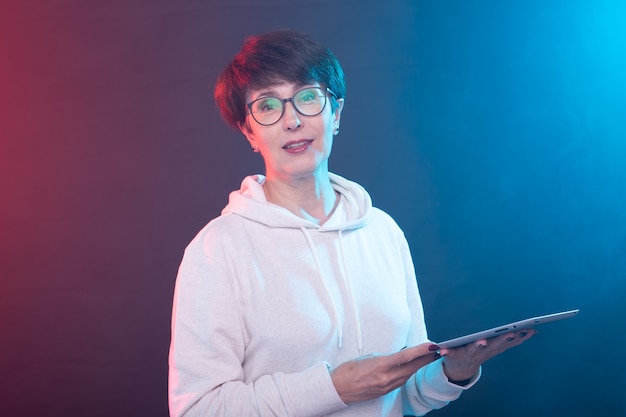 Portrait d'une femme d'âge moyen souriante à l'aide d'un ordinateur tablette sur un mur coloré.