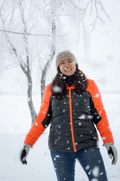 Portrait d'une femme d'âge moyen souriante, chaudement vêtue, debout sur un sol enneigé, regardant la caméra avec des cheveux et un chapeau recouverts de neige Belle période d'hiver pleine de couleurs blanches