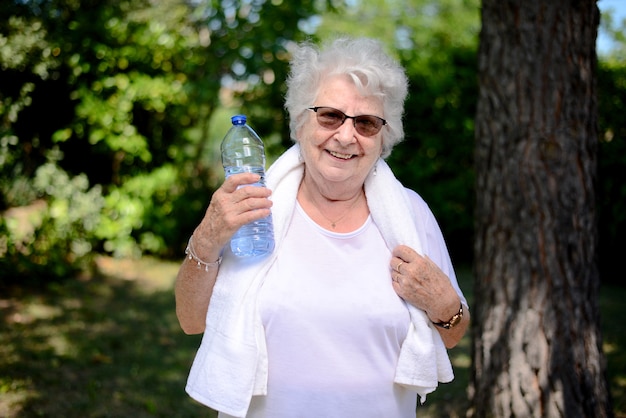 Portrait d'une femme âgée active et dynamique faisant du sport en plein air nature verte et tenant une bouteille d'eau minérale