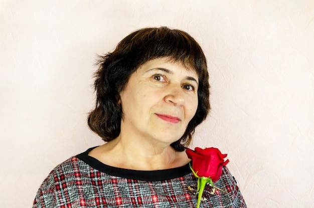 Portrait d'une femme âgée aux cheveux courts foncés Belle femme âgée tenant une rose rouge dans sa main