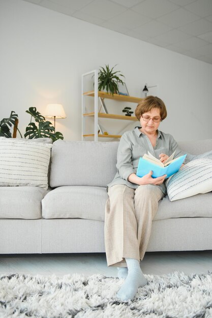 Photo portrait d'une femme âgée détendue assise sur un canapé avec un livre