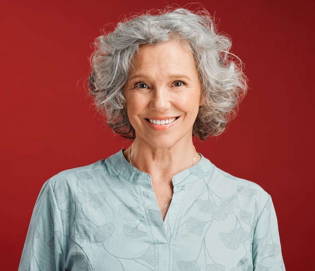 Photo portrait d'une femme âgée heureuse et joyeuse debout sur un fond de studio rouge femme mûre avec des dents blanches et propres en bonne santé montrant la santé bucco-dentaire avec un sourire amical et brillant