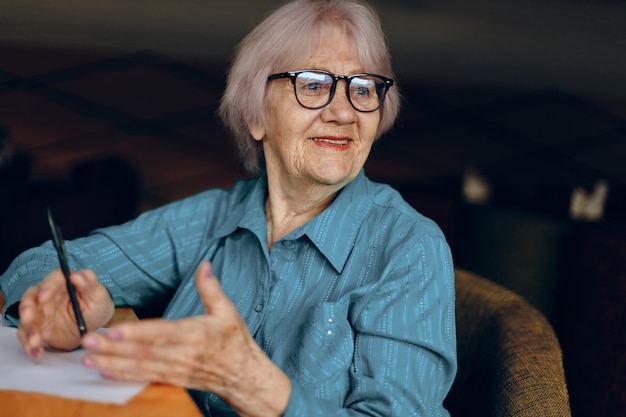 Portrait d'une femme âgée avec des lunettes assise à une table devant un ordinateur portable