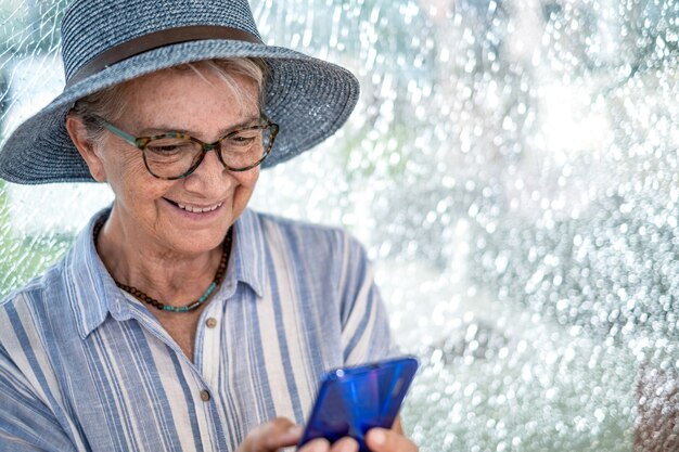 Portrait d'une femme âgée portant un chapeau de paille assis dans un centre commercial souriant et utilisant un téléphone