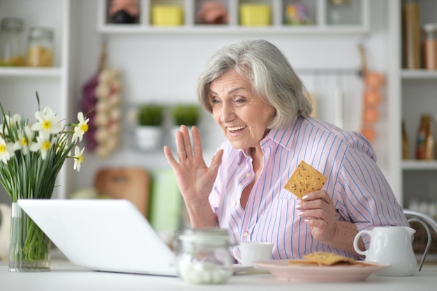 Portrait d'une femme âgée prenant son petit déjeuner avec un ordinateur portable