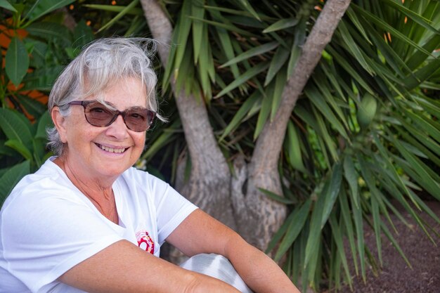 Photo portrait d'une femme âgée souriante assise à côté d'une plante à l'extérieur