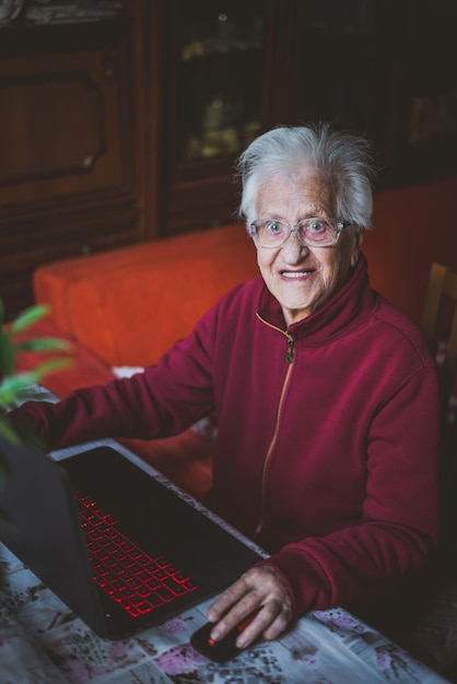 Portrait d'une femme âgée souriante utilisant un ordinateur portable alors qu'elle est assise à la maison