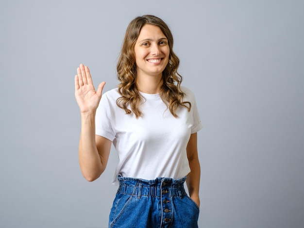 Portrait d'une femme amicale agitant la main pour dire bonjour en vous saluant avec un geste de bonjour