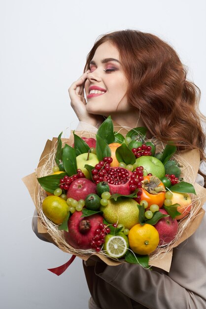 Portrait d'une femme amusante posant un bouquet de fruits vitamines fond clair