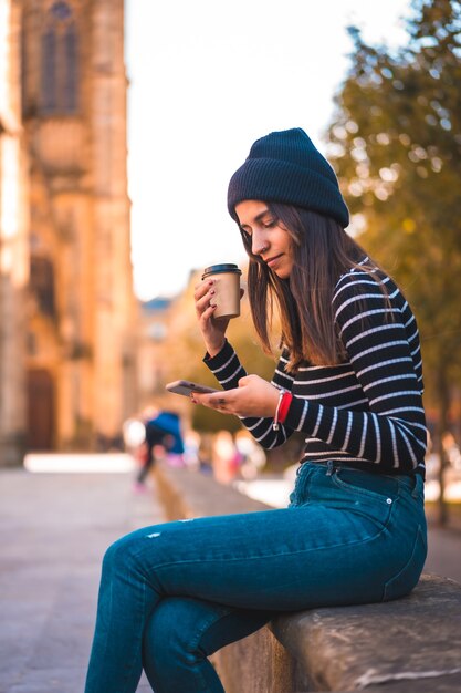 Portrait femme appréciant le café dans le parc tout en utilisant mobile