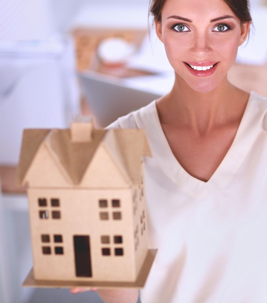 Photo portrait d'une femme architecte tenant une petite maison debout au bureau