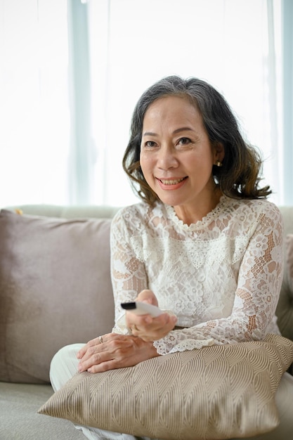 Portrait Une femme asiatique d'âge moyen heureuse regarde la télévision dans son salon confortable