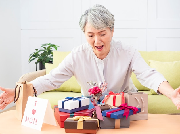 Portrait d'une femme asiatique âgée recevant des coffrets cadeaux et souriant à la maison