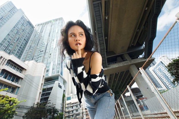 Portrait de femme asiatique des années 20, cheveux bruns, veste haute couture, maquillage sous un nuage de ciel bleu. Belle femme express sentiment émotion sourire heureux sur la gare de chemin de fer