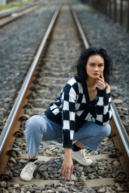 Portrait de femme asiatique des années 20, cheveux bruns, veste haute couture, maquillage sous un nuage de ciel bleu. Belle femme express sentiment émotion sourire heureux sur la gare de chemin de fer