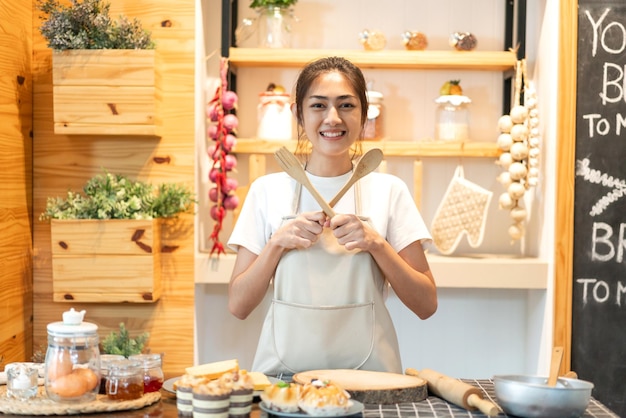 Portrait d'une femme asiatique de beauté professionnelle souriante chef s'amusant à cuisiner avec de la pâte pour des biscuits faits maison et des ingrédients de gâteau sur la table dans la cuisine