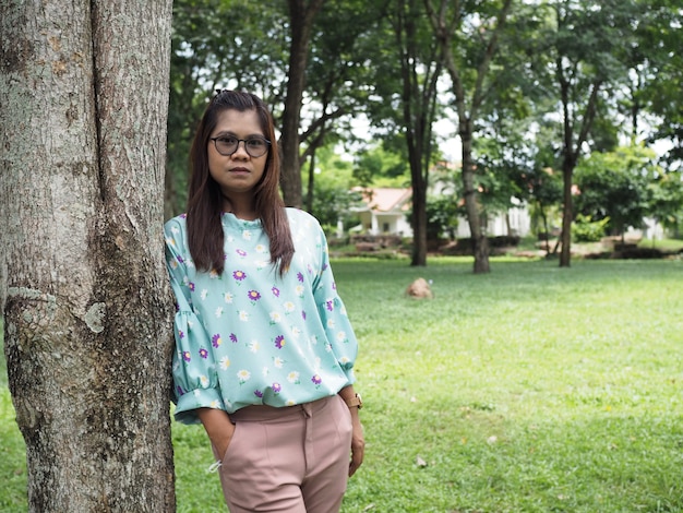 Portrait d'une femme asiatique debout à côté d'un arbre dans le parc Le fond est un arbre vert.