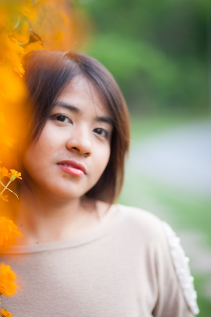 Portrait femme asiatique debout près de fleurs jaunes.