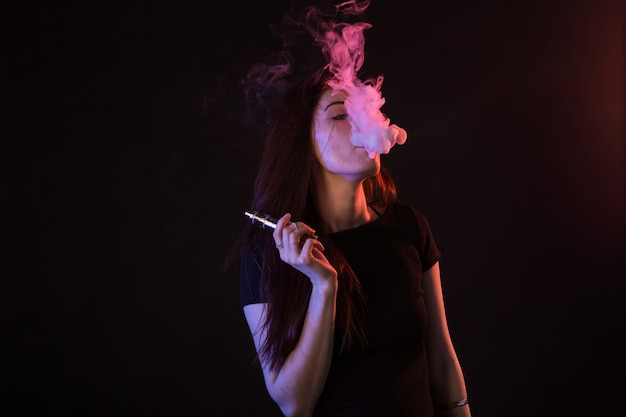 Portrait de femme asiatique fumant vape ou ecigarette en néon sur fond noir.