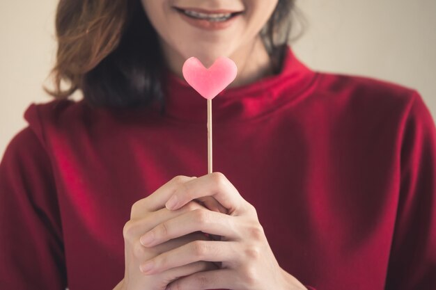 Portrait de femme asiatique heureuse habillée en chandail rouge tenant des bonbons coeur rose.