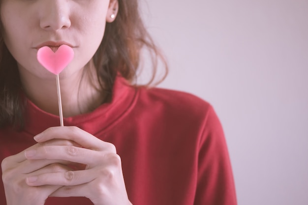 Portrait de femme asiatique heureuse habillée en chandail rouge tenant des bonbons coeur rose.