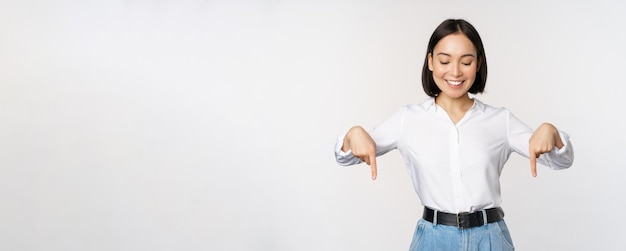 Portrait d'une femme asiatique heureuse pointant les doigts vers le bas et regardant ci-dessous une publicité montrant des informations