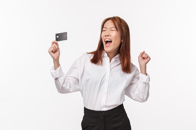 Portrait de femme asiatique heureuse et soulagée réussie crier joyeusement oui, en levant les mains et en applaudissant comme tenant la carte de crédit, fermer les yeux en chantant comme champion,