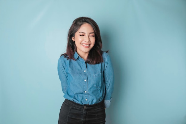 Un portrait d'une femme asiatique heureuse sourit et porte une chemise bleue isolée par un fond bleu