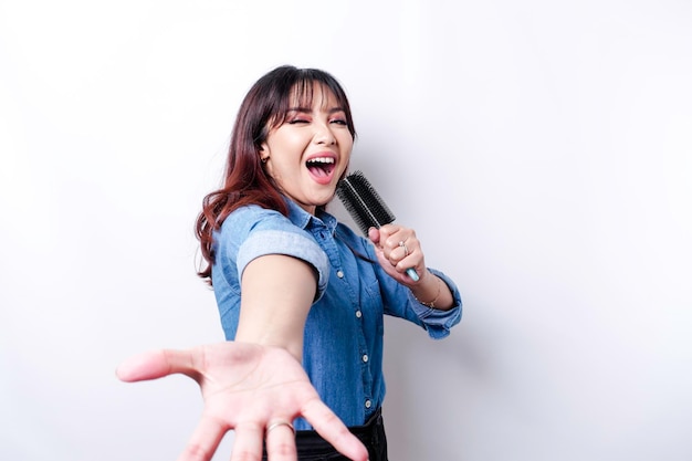 Portrait d'une femme asiatique insouciante s'amusant à chanter au karaoké dans un microphone en se tenant debout sur fond blanc