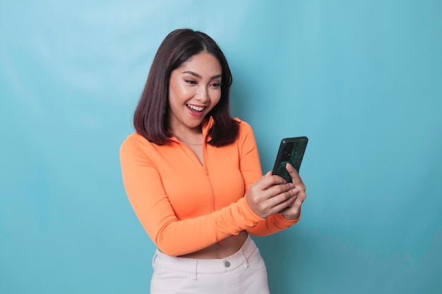 Un portrait d'une femme asiatique joyeuse regardant son smartphone sur fond bleu