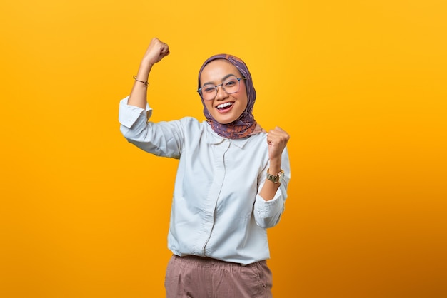 Portrait d'une femme asiatique joyeuse se réjouissant de célébrer la chance sur fond jaune