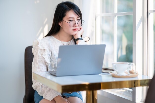 Photo portrait de femme asiatique mécontente, contrariée, frustrée, fronçant les sourcils, indépendante, femme d'affaires, à l'air décontractée, travaillant avec un ordinateur portable, une tasse de café et un smartphone dans un café