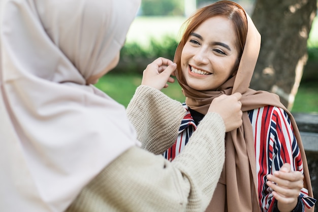 Portrait d'une femme asiatique musulmane heureuse fixant le hijab d'un ami lors d'une réunion en plein air